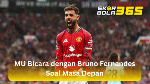 Bruno Fernandes mengenakan jersey kandang merah Manchester United dengan ban kapten, sedang berteriak memberikan instruksi di lapangan dengan logo SKORBOLA365 di pojok kanan atas.