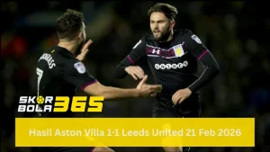 Dua pemain Aston Villa mengenakan jersey hitam dengan detail garis marun (sponsor Unibet) sedang berinteraksi di lapangan; pemain di kanan (Henri Lansbury) tampak berteriak memberikan instruksi atau merayakan momen dengan tangan terbuka, sementara pemain di kiri membelakangi kamera; terdapat logo SKOR BOLA 365 di pojok kiri bawah dan teks "Hasil Aston Villa 1-1 Leeds United 21 Feb 2026" pada bilah kuning di bagian bawah.