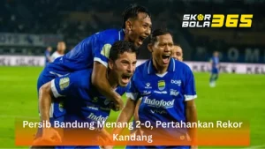 Tiga pemain Persib Bandung mengenakan jersey biru kebanggaan sedang merayakan gol dengan sangat ekspresif; satu pemain menggendong rekannya sementara pemain lainnya berteriak gembira di depan kamera, terdapat logo SKORBOLA365 di pojok kanan atas dan teks "Persib Bandung Menang 2-0, Pertahankan Rekor Kandang" pada bilah oranye transparan di bagian bawah.