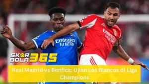 Duel fisik antara pemain Real Madrid (Vinicius Jr) mengenakan jersey biru gelap dengan pemain Benfica mengenakan jersey merah (Elias Jelert) yang berusaha menahan laju serangan dengan tangan; latar belakang stadion yang penuh penonton; terdapat logo SKOR BOLA 365 kuning di pojok kiri tengah dan teks "Real Madrid vs Benfica: Ujian Los Blancos di Liga Champions" pada bilah kuning di bagian bawah.