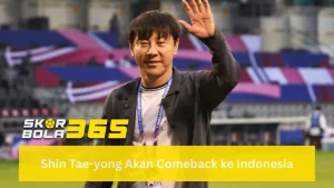 Foto pelatih Shin Tae-yong sedang tersenyum ramah dan melambaikan tangan kanan ke arah kamera di area stadion; ia mengenakan jaket biru navy di atas kaos putih; terdapat logo SKORBOLA365 di pojok kiri bawah dan teks "Shin Tae-yong Akan Comeback ke Indonesia" pada bilah kuning cerah di bagian bawah.